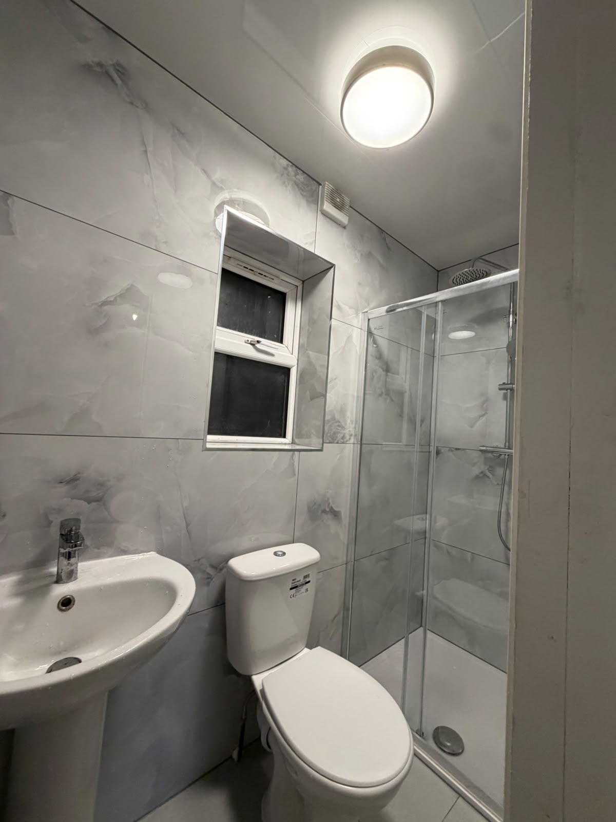 Completed bathroom with basin, toilet and glass shower enclosure